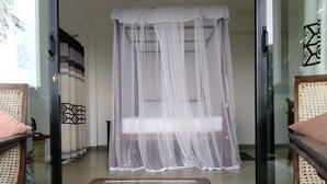 A room with a glass partition, a bed with a white canopy, and wicker furniture. - Lara's Place Unawatuna (Unawatuna)