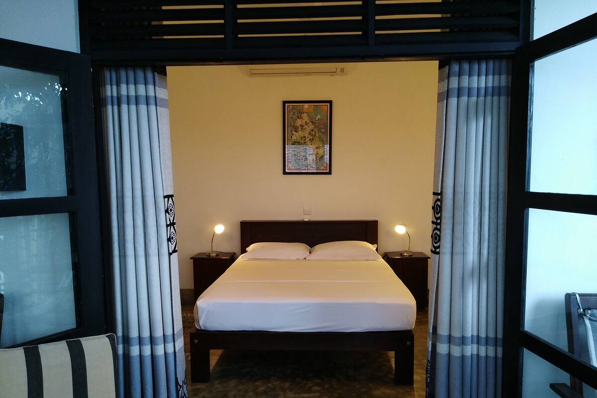 A hotel room with a bed, two bedside tables with lamps, a map on the wall, and curtains.