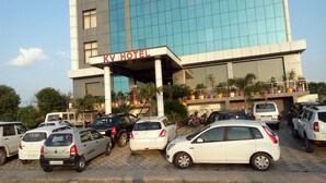 Un hotel con fachada moderna de vidrio, entrada cubierta y estacionamiento con varios coches.