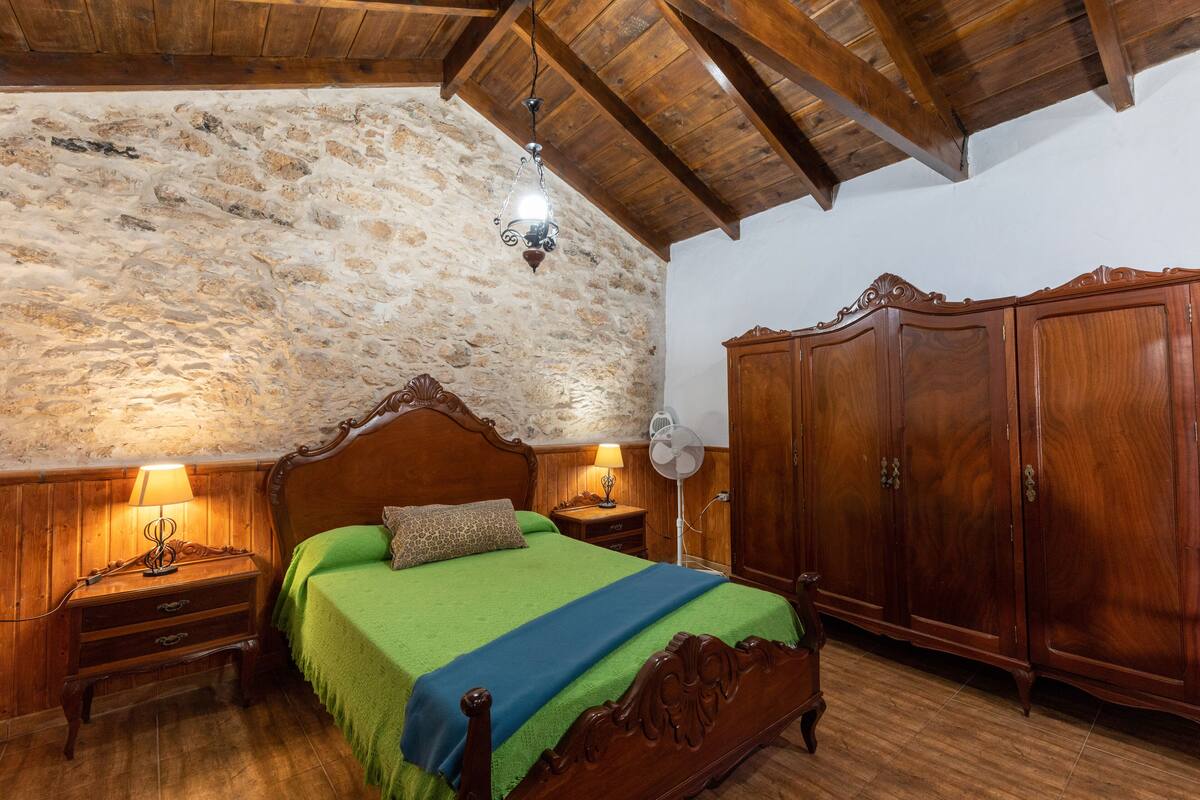 Ein Schlafzimmer mit Steinwand, Holzboden und einem großen Kleiderschrank. Es gibt ein Bett mit grüner Bettwäsche und zwei Nachttischlampen.