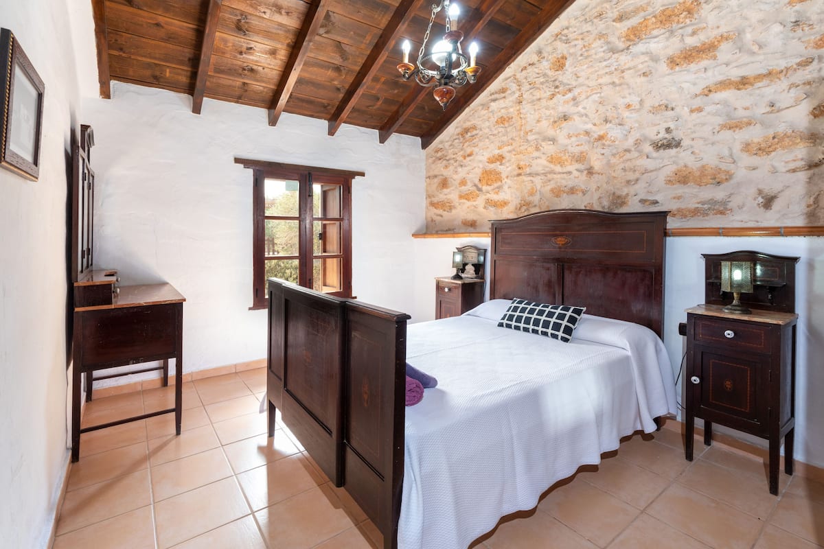 Ein Schlafzimmer mit einem hölzernen Bett, einem Nachttisch, einer Kommode und einer Steinwand.