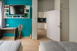 Moderni makuuhuone, jossa on kaksi sänkyä, televisio ja taustalla pieni keittiönurkkaus.