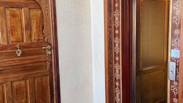 Une porte en bois ornée de sculptures complexes et dotée d’une poignée en métal, un sol en marbre à carreaux et un mur à motifs.