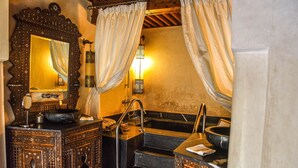 Ein traditionelles Badezimmer mit einem großen, verzierten Spiegel, einer Badewanne und einem Waschbecken mit dekorativen Schränken.