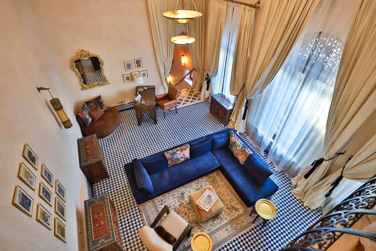 Uma sala de estar ampla com um sofá azul, tapetes estampados e piso xadrez.