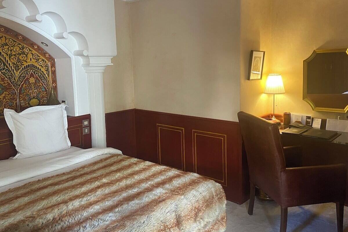 Quarto de hotel com uma cama grande, uma escrivaninha com cadeira, uma luminária e um quadro na parede.