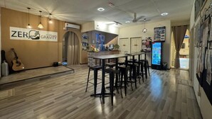 A modern bar area with a wooden floor, black bar stools, and a guitar. There is a sign that reads "ZERO GRAVITY" and a refrigerator with a drink dispenser. - The Village (Semporna)