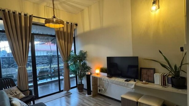 A modern living room with a sofa, TV, and a balcony with curtains. - The Village (Semporna)