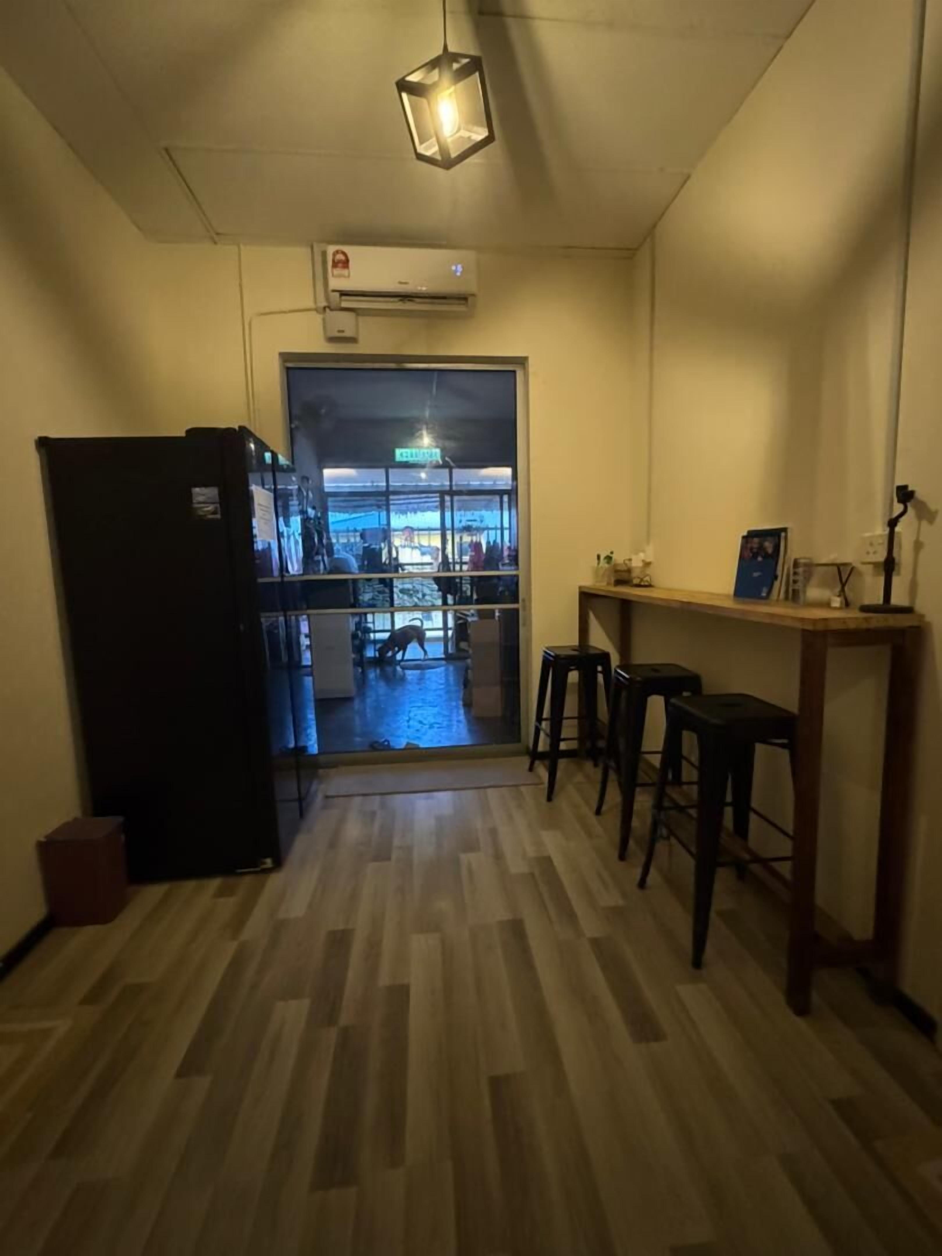 A narrow hallway with a wooden floor, a black refrigerator, and a small table with stools.