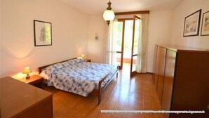 A bedroom with a bed, bedside table, lamp, and a view of the outside. - Lignano Riviera Spacious (Lignano Sabbiadoro)