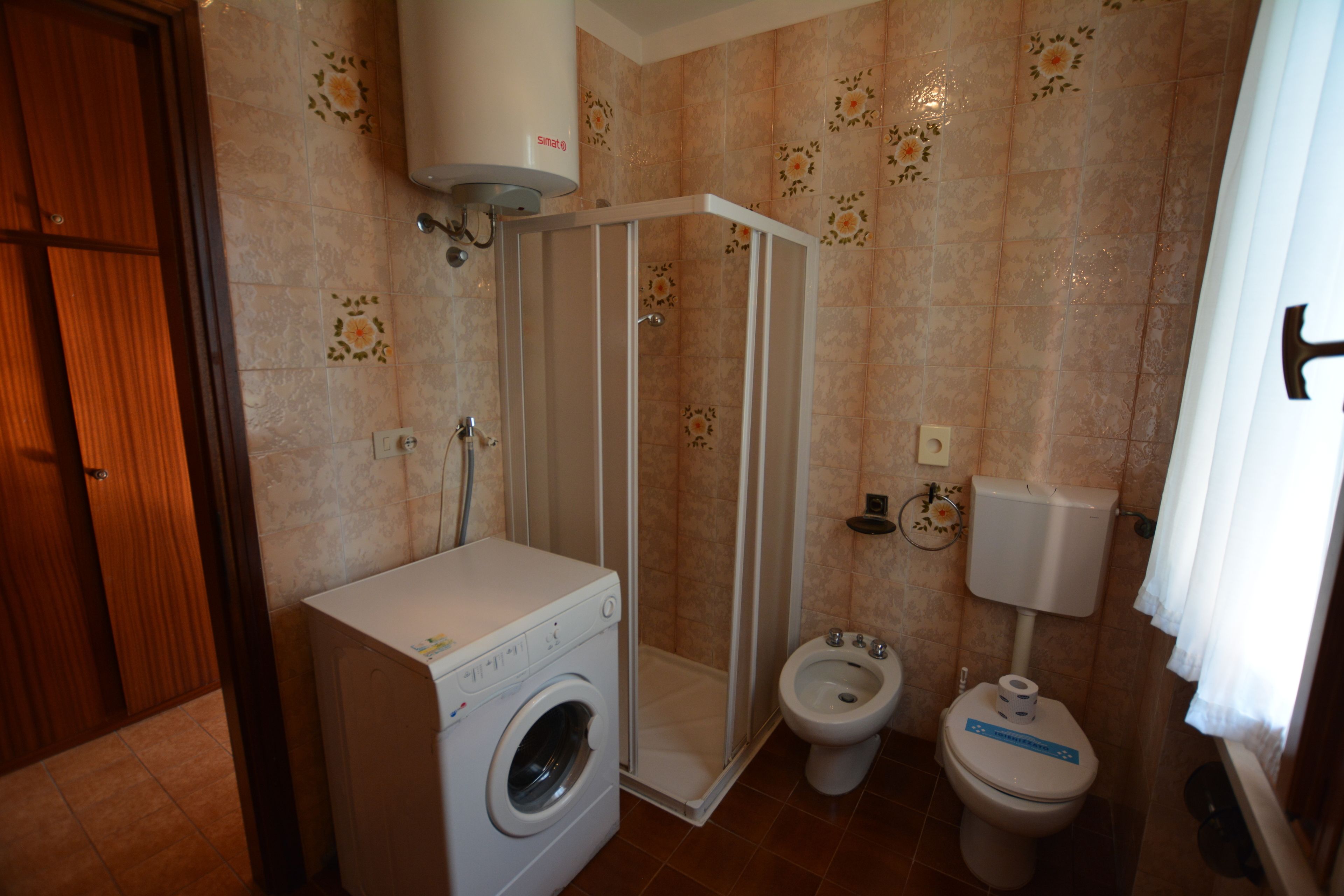 Een badkamer met een douchecabine, toilet en wasmachine.