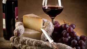 A cheese, grapes, a knife, and a wine bottle on a wooden surface. - Lignano Riviera Spacious (Lignano Sabbiadoro)
