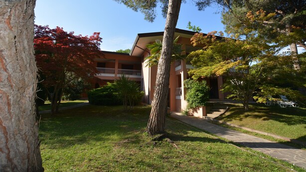 A building with a balcony, surrounded by trees and a lawn. - Lignano Riviera Spacious (Lignano Sabbiadoro)