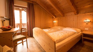 A wooden cabin room with a bed, a chair, a table with a fruit bowl, and two wall-mounted lamps.