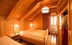 A wooden cabin bedroom with a large bed, two bedside tables, and a window with curtains.