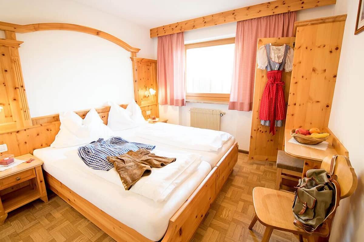 Une pièce en bois comprenant un lit, une table de chevet, une chaise, une table et une fenêtre avec des rideaux.