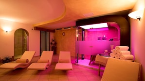 A spa room with four lounge chairs, a table with towels, and a pink-lit massage area.