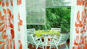A dining area with a table set for two, surrounded by white chairs, and a view of greenery through the window. - Lignano with pool (Lignano Sabbiadoro)