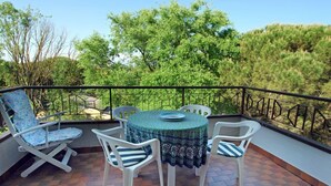 A balcony with a round table and four chairs, surrounded by a black metal railing. - Lignano with pool (Lignano Sabbiadoro)