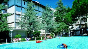 A swimming pool area with a building in the background. - Lignano with pool (Lignano Sabbiadoro)