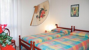 A bedroom with two wooden beds, a hanging fan, a poster on the wall, and a chair with a red cushion. - Villa in Lignano Riviera Comfortable (Lignano Sabbiadoro)