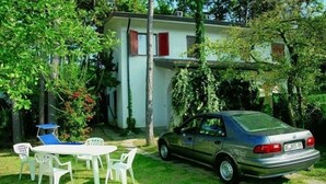 A car parked in a grassy area with a white building in the background, surrounded by trees and greenery. - Villa in Lignano Riviera Comfortable (Lignano Sabbiadoro)