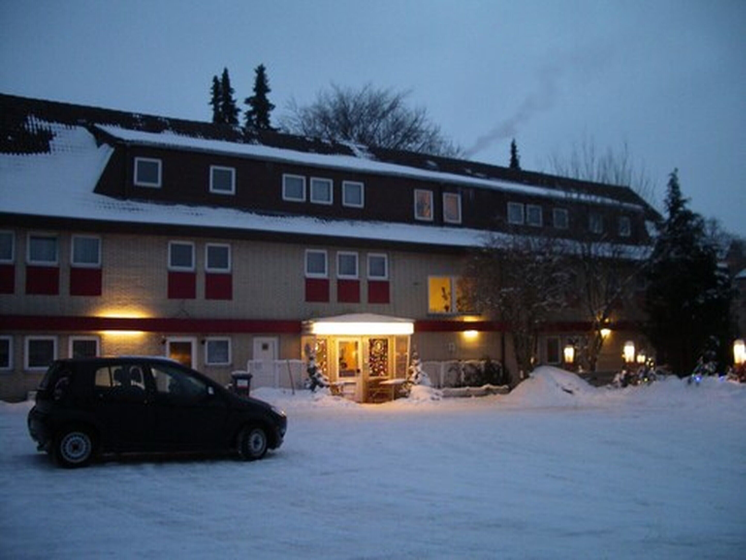 A hotel with a snow-covered roof, multiple windows, and a car parked in front.
