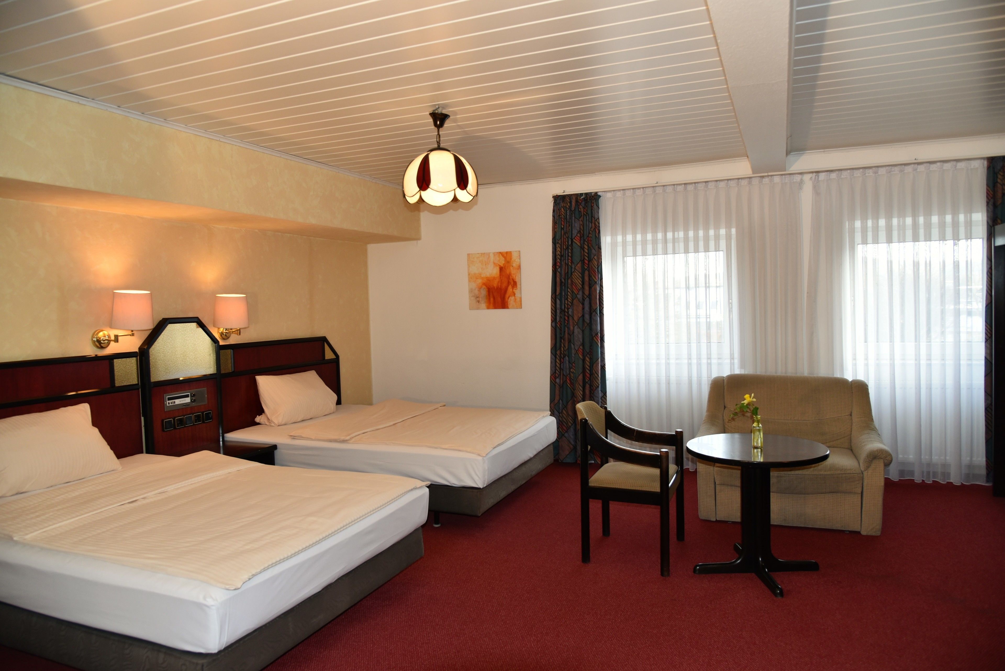 A hotel room with two beds, a sofa, a small table, and a ceiling light fixture.