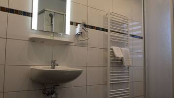 Une salle de bain moderne avec un lavabo blanc, un miroir, un porte-serviettes et une cabine de douche en verre.