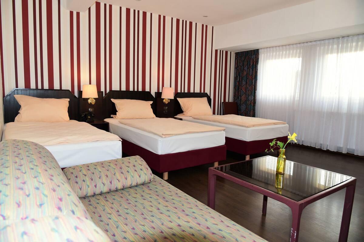 A hotel room with two beds, a sofa, a glass coffee table, and a striped wall.