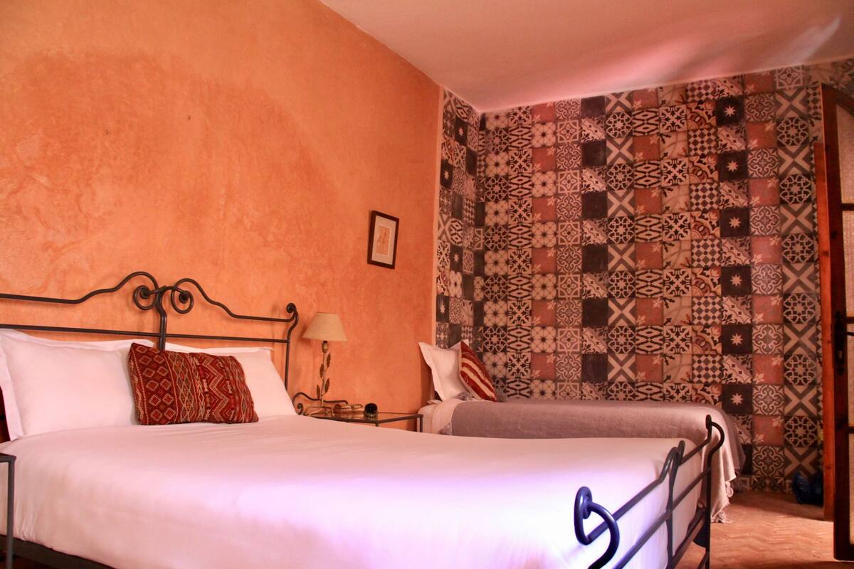 Una habitación con dos camas, un papel tapiz estampado y un cuadro en la pared.