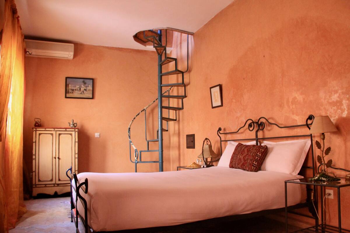 Un dormitorio con una cama, una escalera espiral de metal, un armario y una mesita de noche.