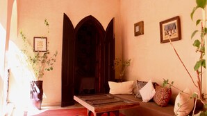A room with a wooden table, a sofa with cushions, a large potted plant, and a door with an arched design. - Riad Dama (Marrakech)