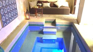 A swimming pool with steps leading into it, a bench, and a small table with a lantern. - Riad Dama (Marrakech)