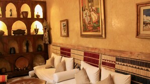 A traditional room with a sofa, wall-mounted shelves with decorative items, and a large painting. - Riad Dama (Marrakech)