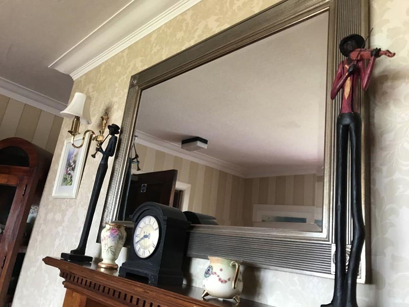 A room with a large mirror, a clock, and a vase on a mantelpiece.