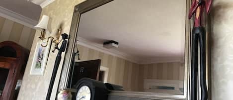 A room with a large mirror, a clock, and a vase on a mantelpiece.
