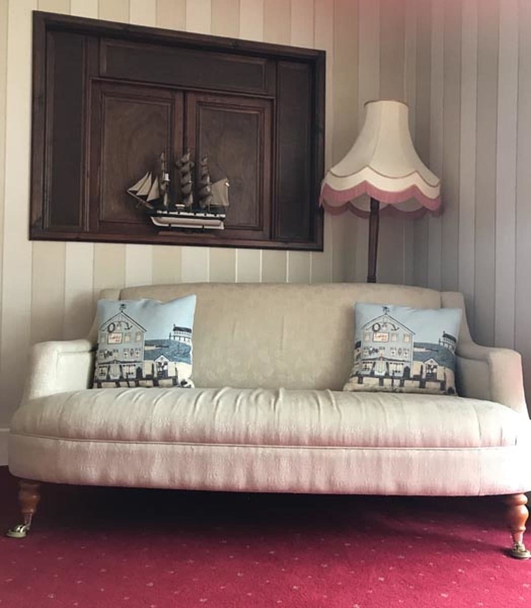 A beige sofa with two decorative pillows, a dark wooden cabinet above, and a white lamp with a pink shade to the right.