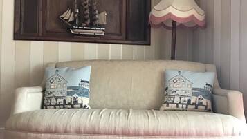 A beige sofa with two decorative pillows, a dark wooden cabinet above, and a white lamp with a pink shade to the right.