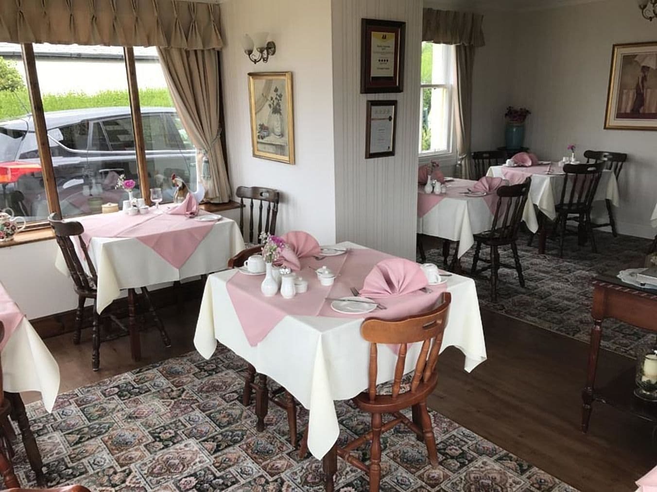 Comedor con mesas dispuestas para el servicio, alfombra estampada y sillas de madera.