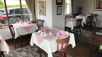 Comedor con mesas dispuestas para el servicio, alfombra estampada y sillas de madera.