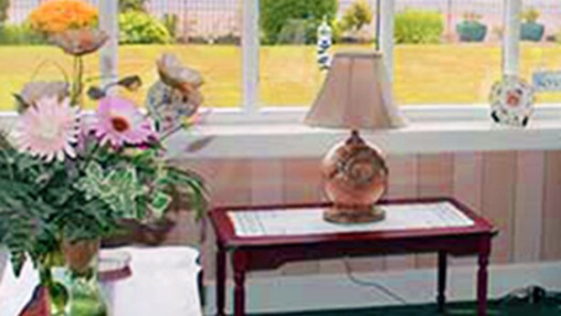 Une pièce avec une grande fenêtre, un vase rempli de fleurs, une lampe et une petite table.
