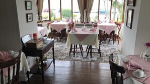 Un espace repas avec plusieurs tables dressées, un bureau en bois avec un ordinateur et des tableaux encadrés accrochés aux murs.