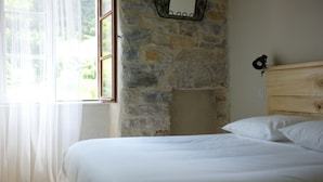 A bedroom with a stone wall, a wooden headboard, and a window with sheer curtains.