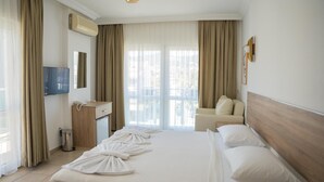 A hotel room with a bed, a desk, a chair, a TV, and a balcony with curtains. - Muse No:1 (Marmaris)