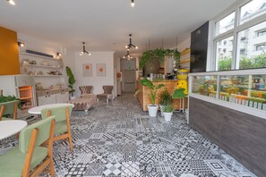 Ein modernes Café mit gemusterten Bodenfliesen, Holzmöbeln und verschiedenen Pflanzen.