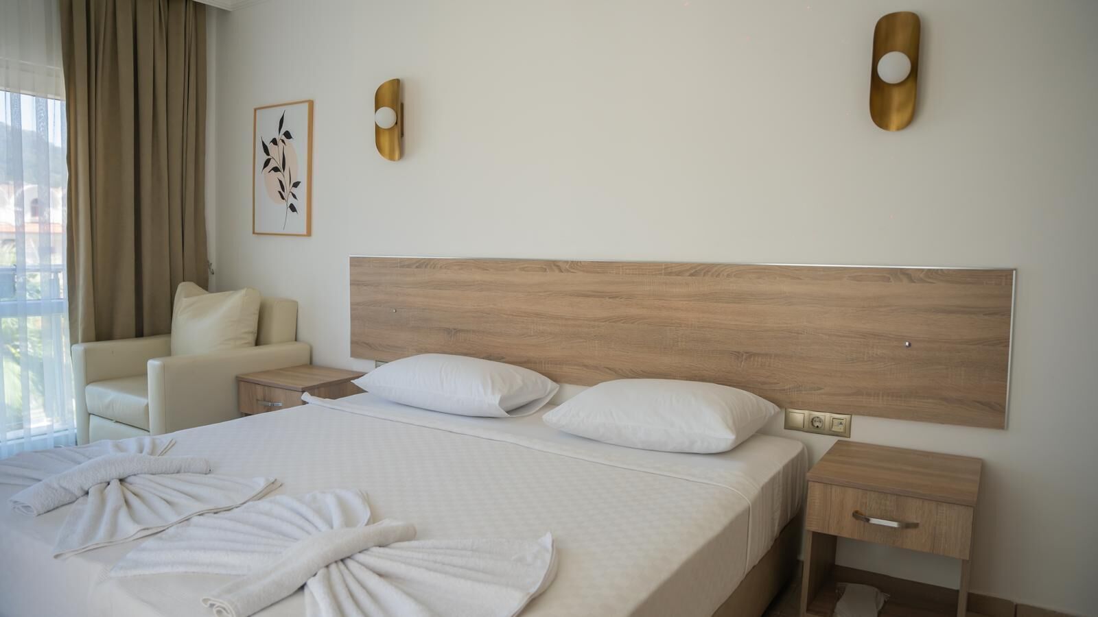 A hotel room with a large bed, two bedside tables, a chair, and a wall-mounted light fixture.