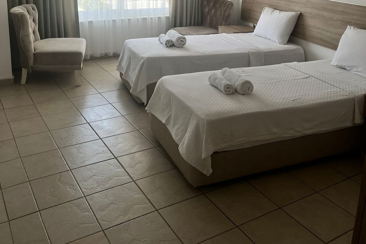 Ein Hotelzimmer mit zwei Betten, einem Sessel und Blick auf Grün hinter dem Fenster.