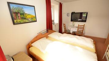 Quarto com cama, televisão, escrivaninha com cadeira e um quadro na parede.