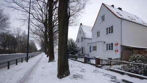 A snow-covered street with a white building featuring a sign for a bed and breakfast. - Airportgästehaus Bremen (Bremen)